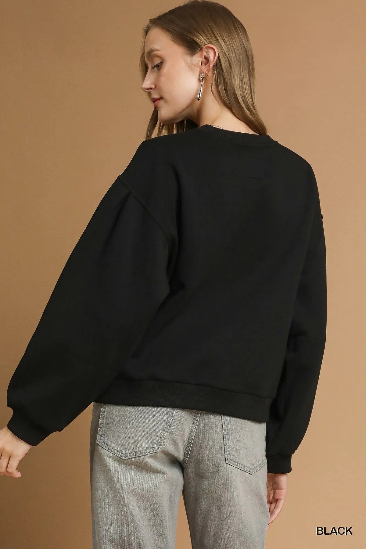 Rear view of black pleated round neck sweatshirt showing relaxed fit silhouette and continuous ribbed hemline against a solid