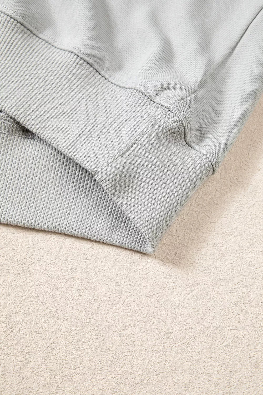 Detail view of bottom hem showcasing wide ribbed waistband construction and double-needle stitching on solid light grey