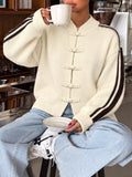 Modelin creamfarbener Strickjacke mit Chinesischen Knotenknöpfen und braunen Seitenstreifen, die eine Tasse hält
