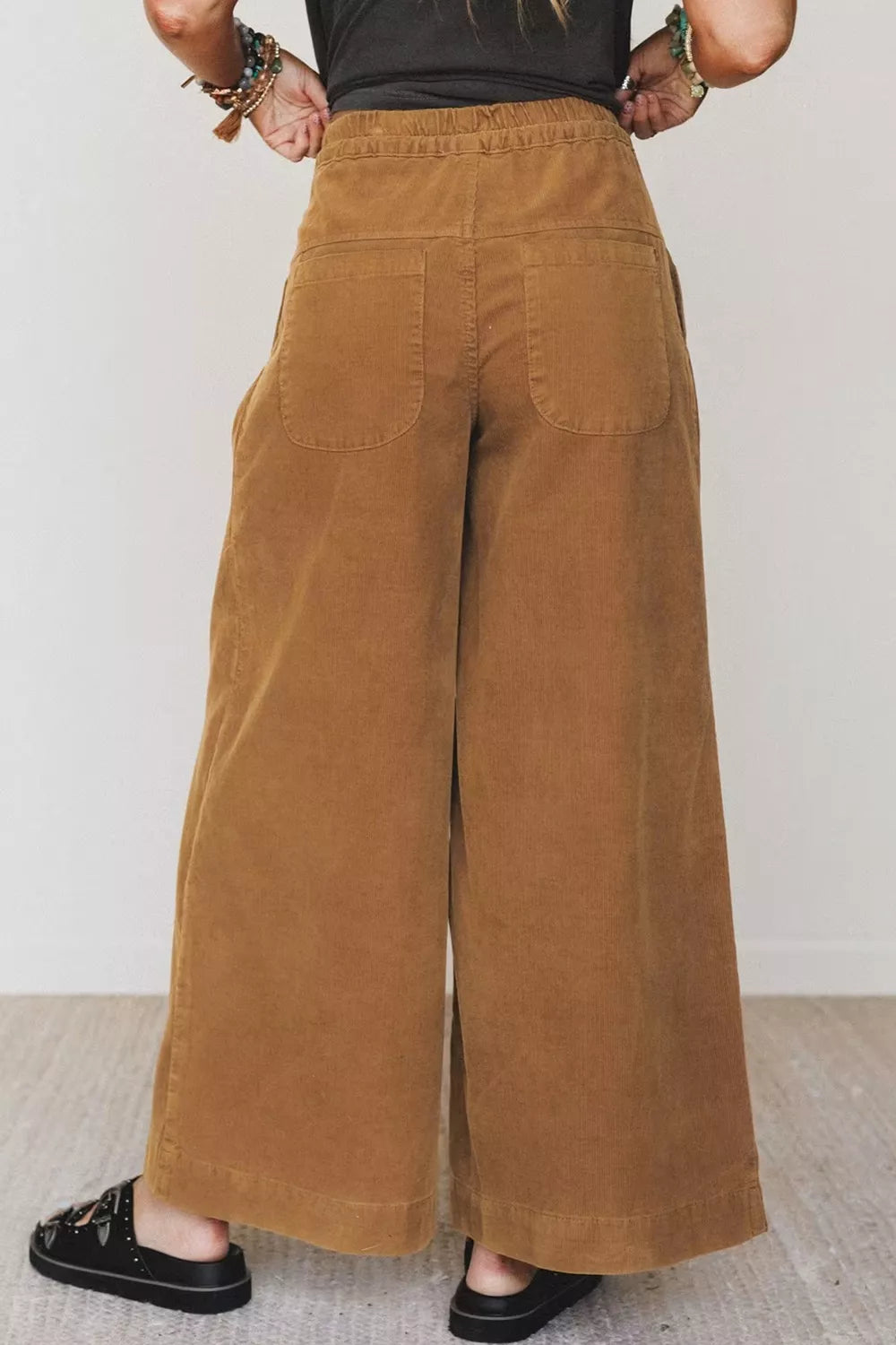 Vista trasera de pantalones de pana camel de pierna ancha mostrando bolsillos parche y cintura elástica ajustada sobre fondo blanco