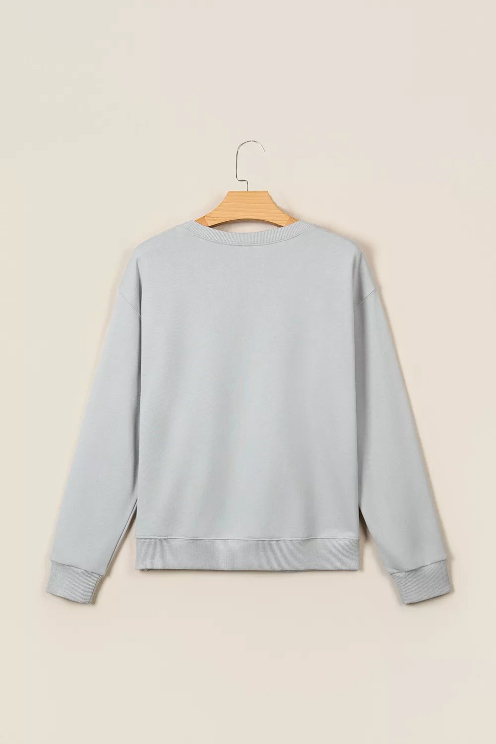 Back view of light grey long-sleeve sweatshirt on wooden hanger. Plain design features ribbed cuffs and hem against neutral