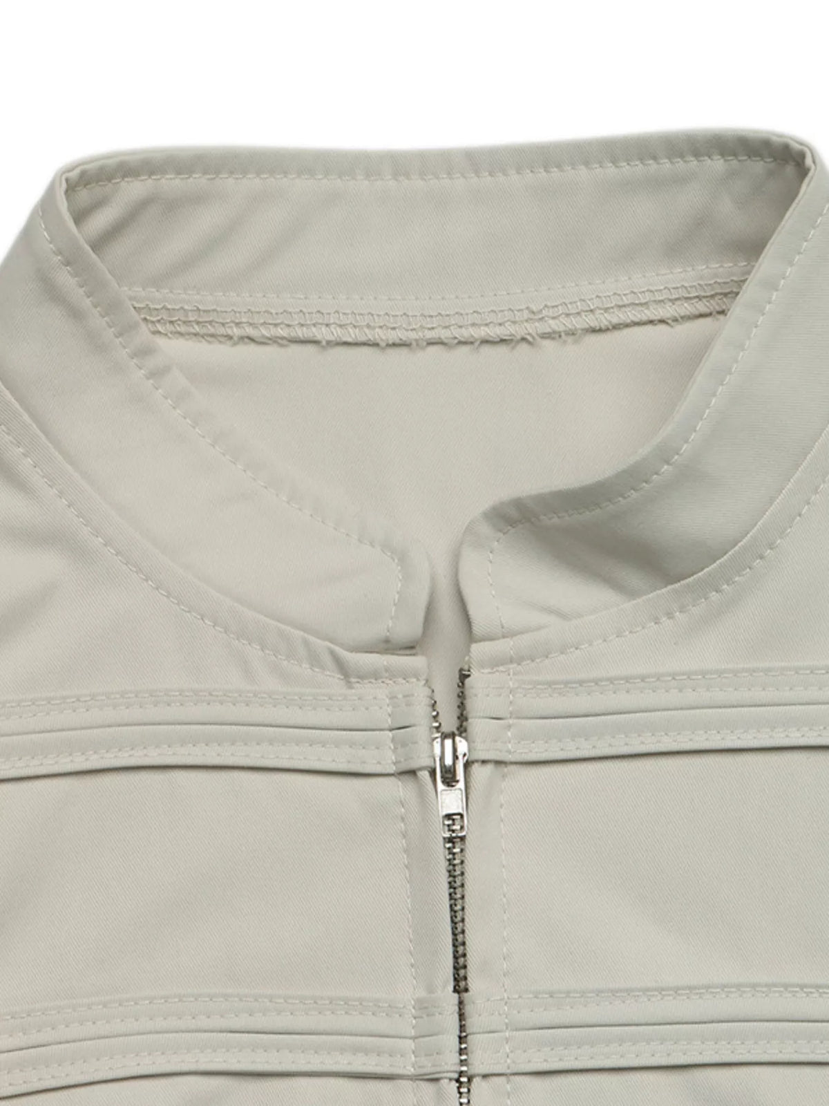 Détail du col mandarin haut et de la patte de boutonnage zippée argentée sur vêtement extérieur beige clair