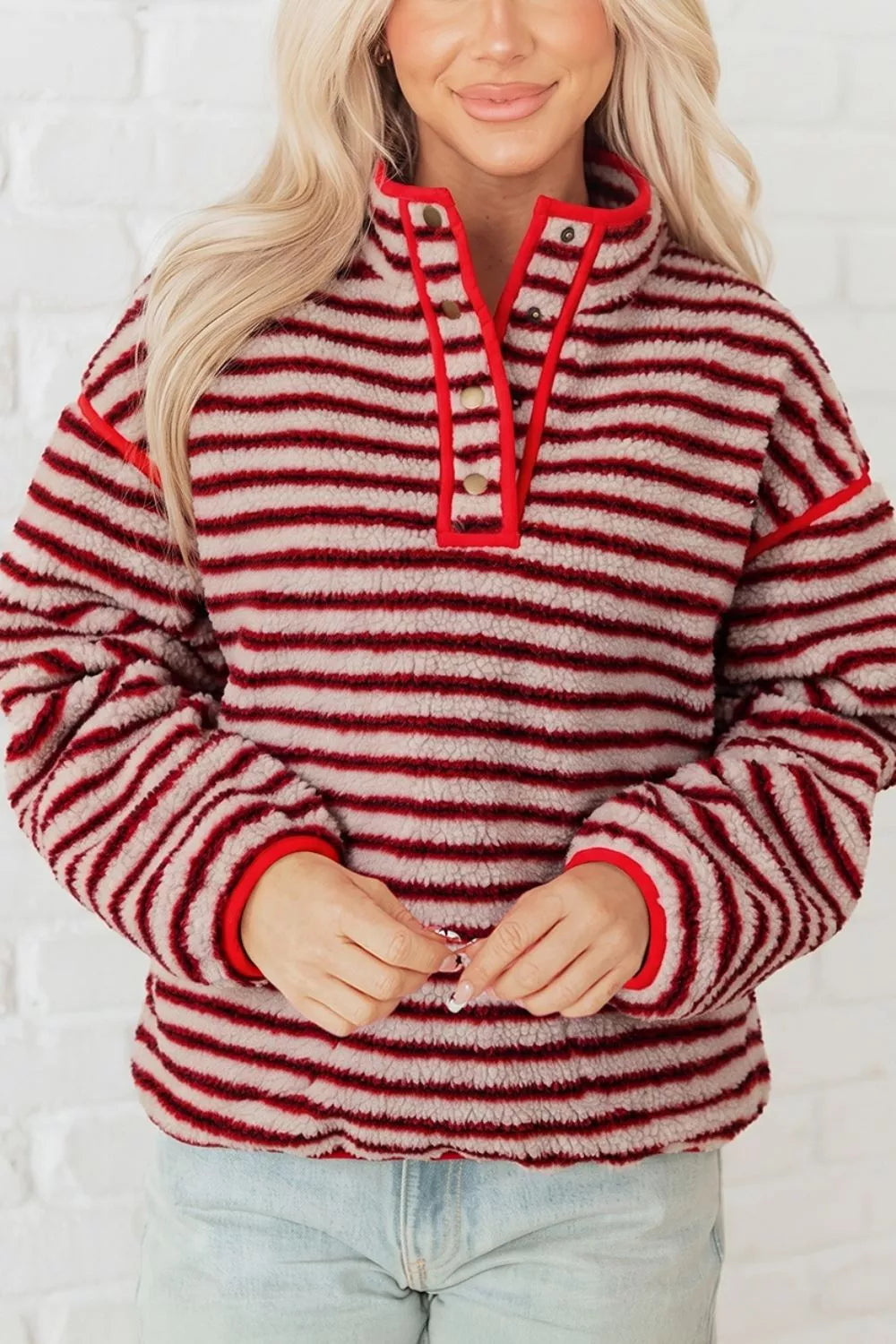 Sudadera pullover sherpa roja y crema de corte holgado, media solapa de cuatro botones frente a pared blanca