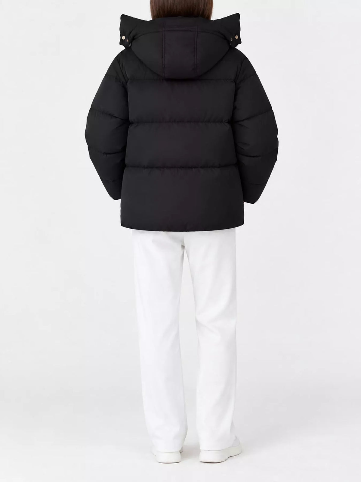 Back view of model in black quilted hooded puffer jacket with horizontal stitching and white pants