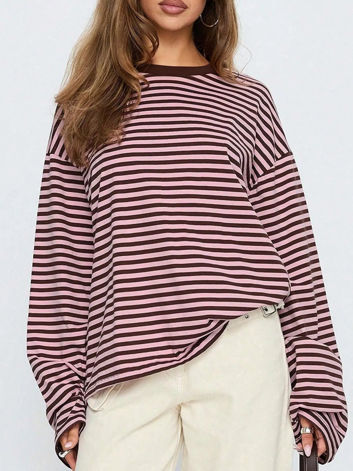 Frontale modella in maglietta maniche lunghe a righe marrone e rosa antico con pantaloni crema e orecchini a cerchietto argento