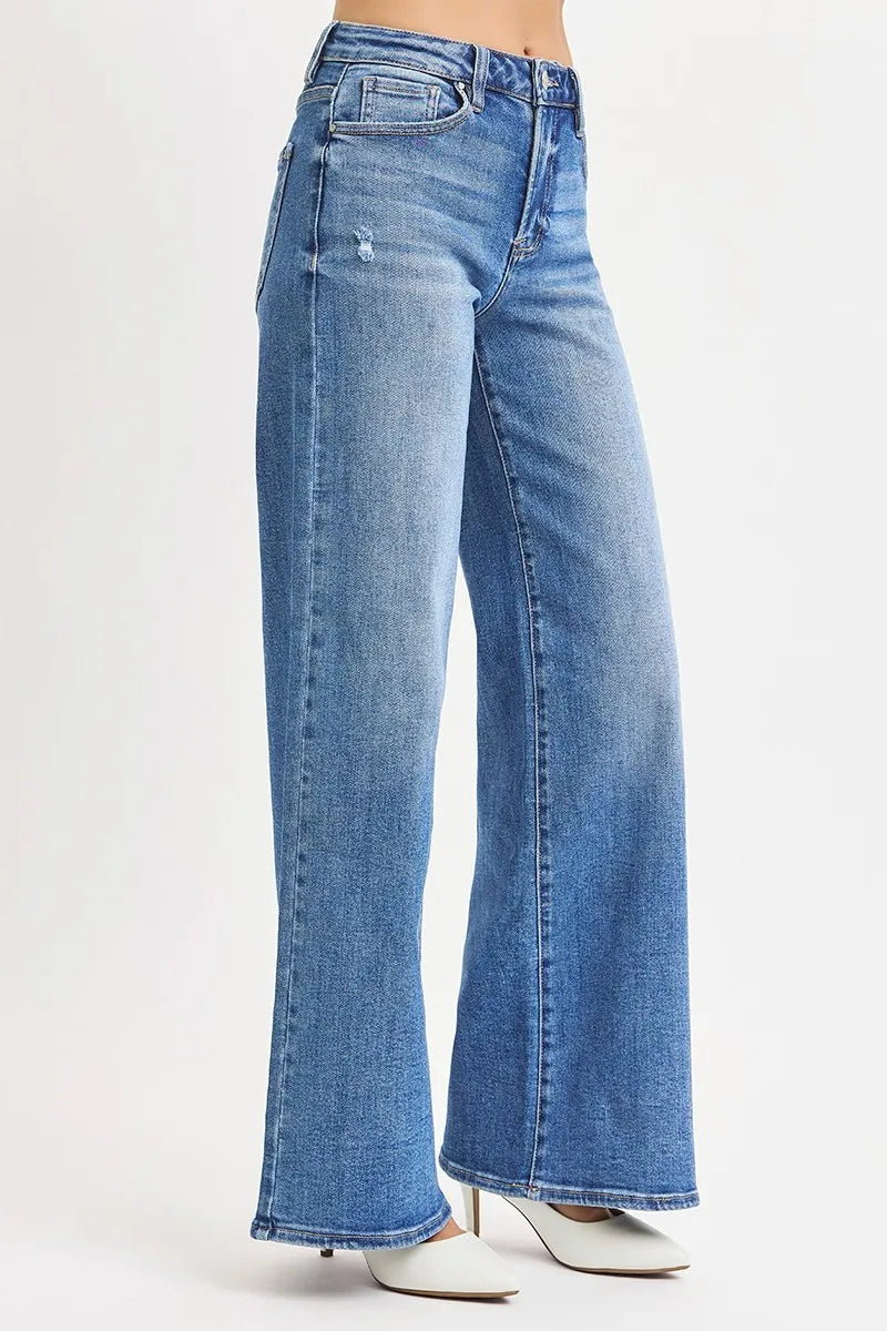 Side profile of high-waisted wide-leg jeans emphasizing straight thigh silhouette and small side rip detail with white heels