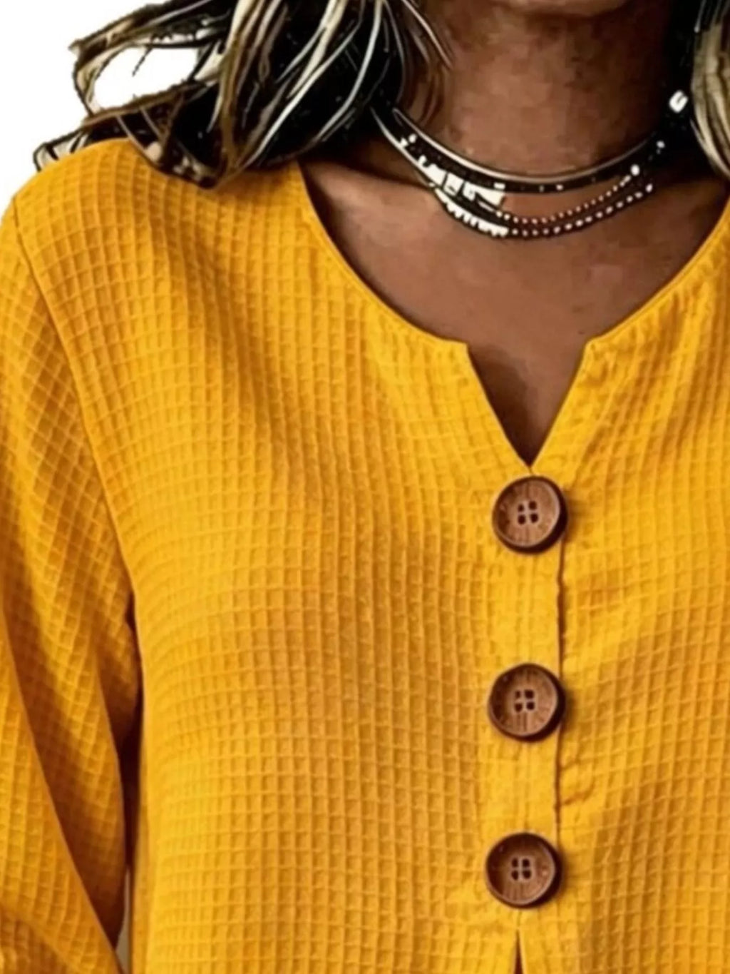 Detalle del escote en V del top amarillo con tres botones de madera marrones visibles