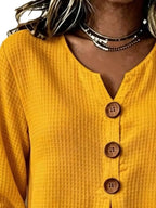 Detalle del escote en V del top amarillo con tres botones de madera marrones visibles