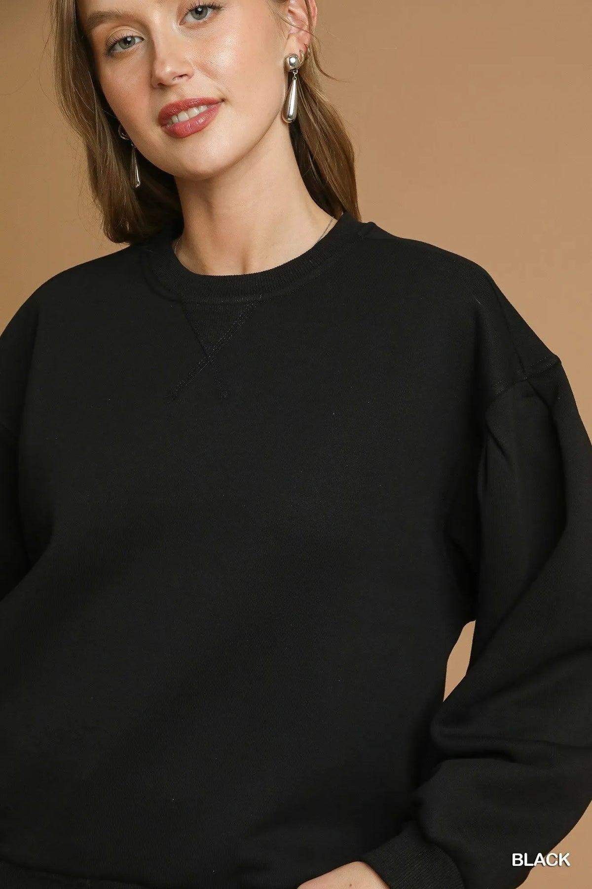 Close-up of black pleated round neck sweatshirt neckline highlighting textured V-shaped pleated stitching triangle below the