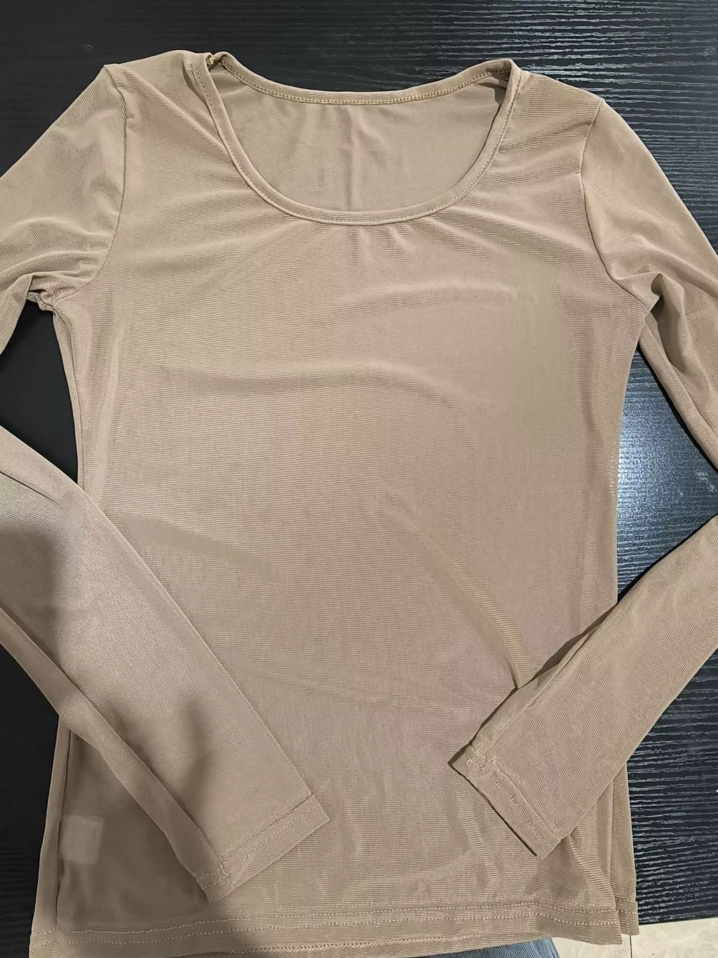 Nude colored mesh top on dark wood surface highlighting scoop neck and semi-transparent ribbing