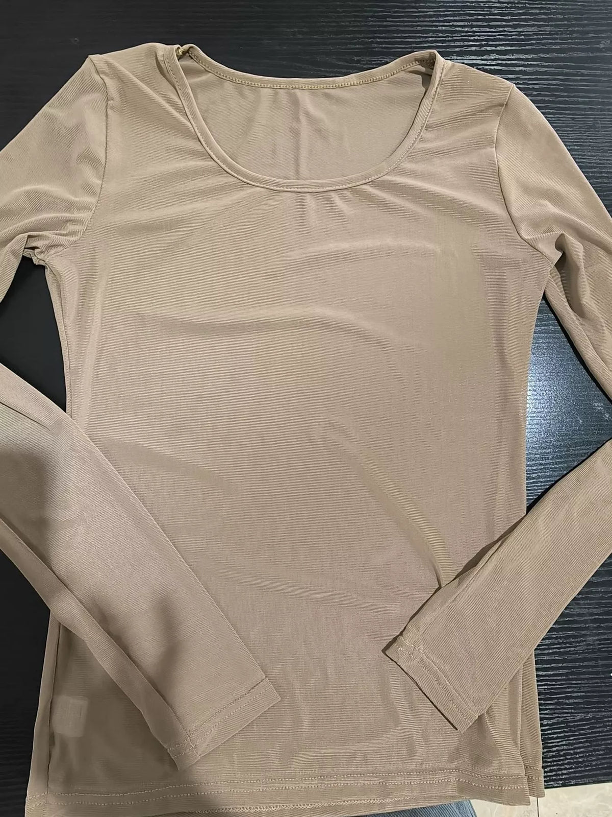 Nude colored mesh top on dark wood surface highlighting scoop neck and semi-transparent ribbing