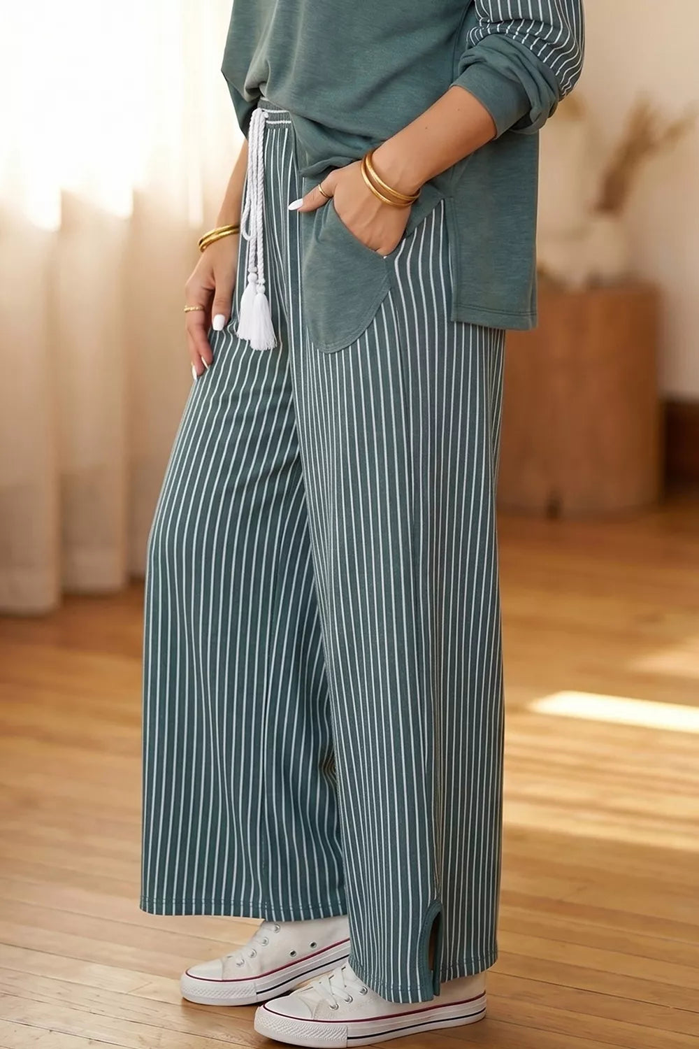 Seitendetail der teal Hose mit weißem Quasten-Kordelzug, Patch-Tasche und Knöchelschlitz über Sneakers