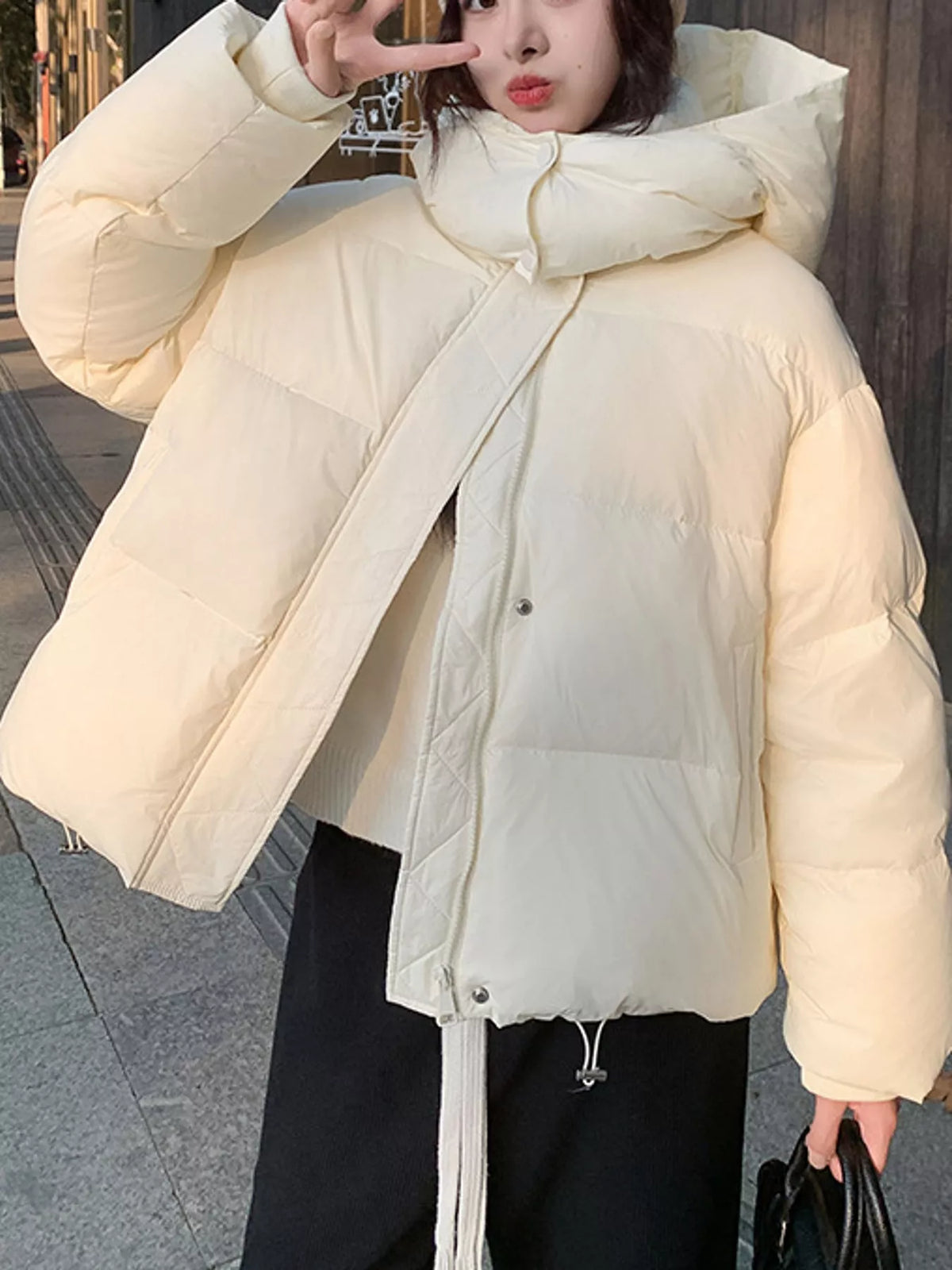 Model in cream-colored quilted puffer jacket standing outdoors making peace sign gesture near face