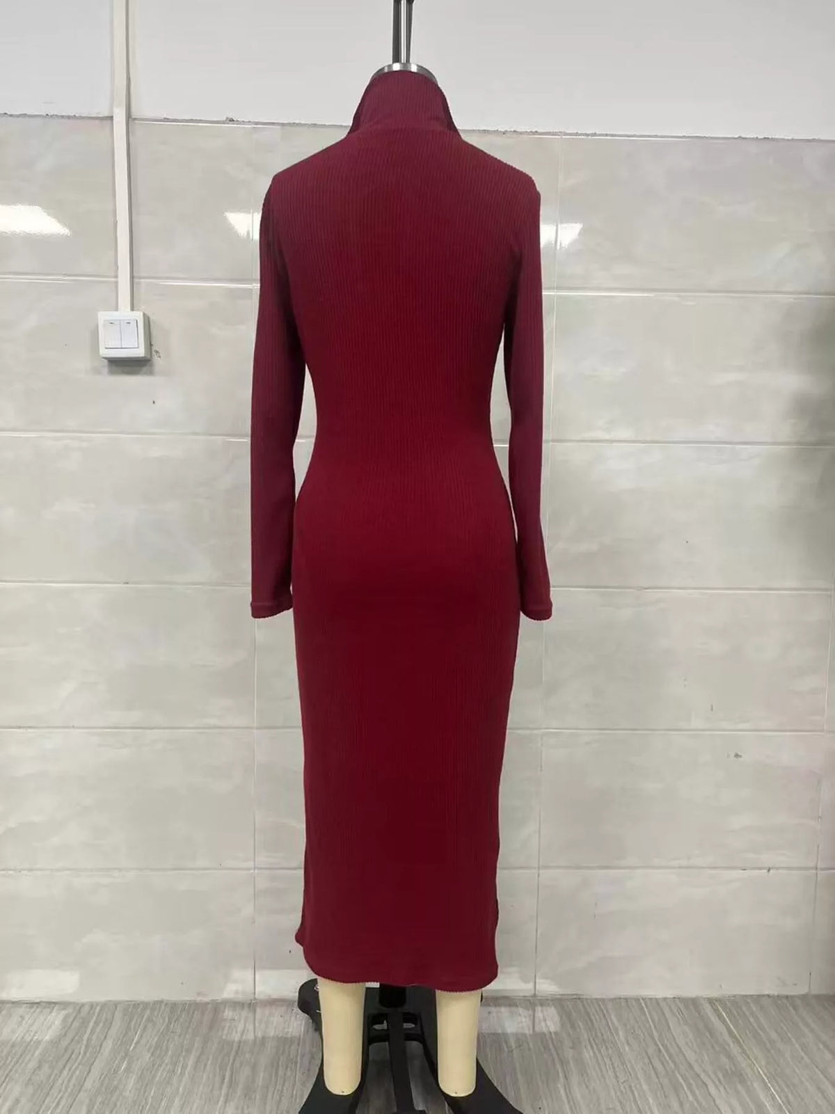 Vue arrière d'une robe pull tricotée côtelée bordeaux sur mannequin insistant sur les côtes verticales lisses et la coupe ajustée jusqu'aux hanches