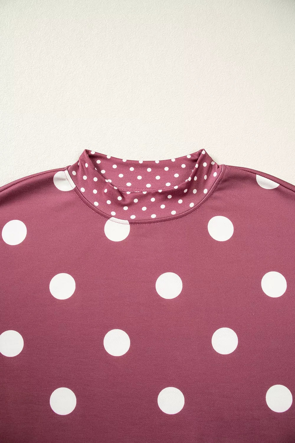 Close up of mock neck collar with small white polka dots contrasting against large dots on maroon fabric
