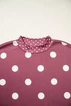 Close up of mock neck collar with small white polka dots contrasting against large dots on maroon fabric