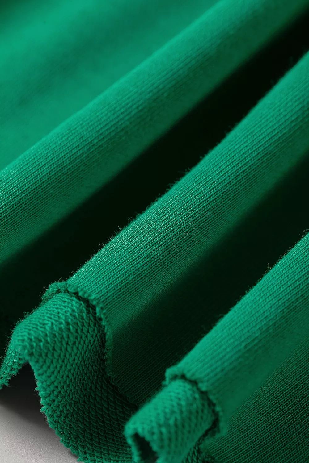 Vista detallada de capas textiles verdes: acabado superficial suave y borde de tela sin rematar. Calidad en cada detalle.