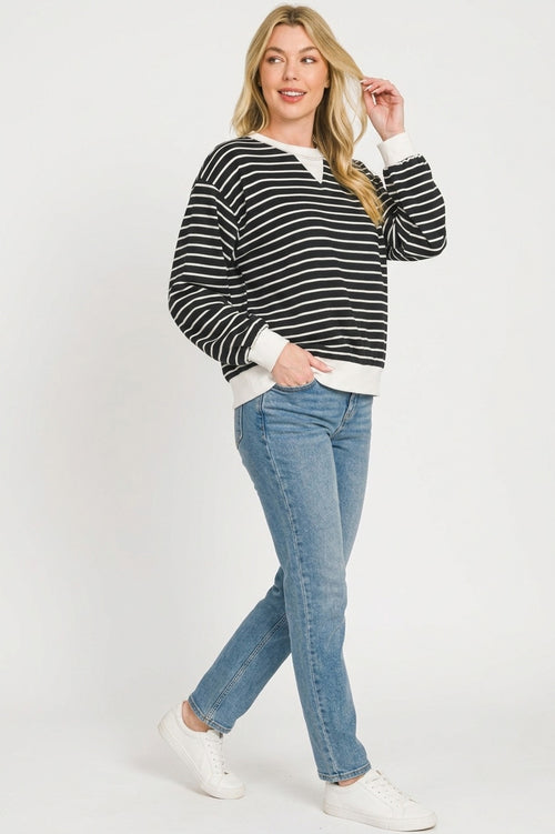 Model wearing relaxed fit black and white striped sweatshirt with light jeans and white sneakers in full-body front view