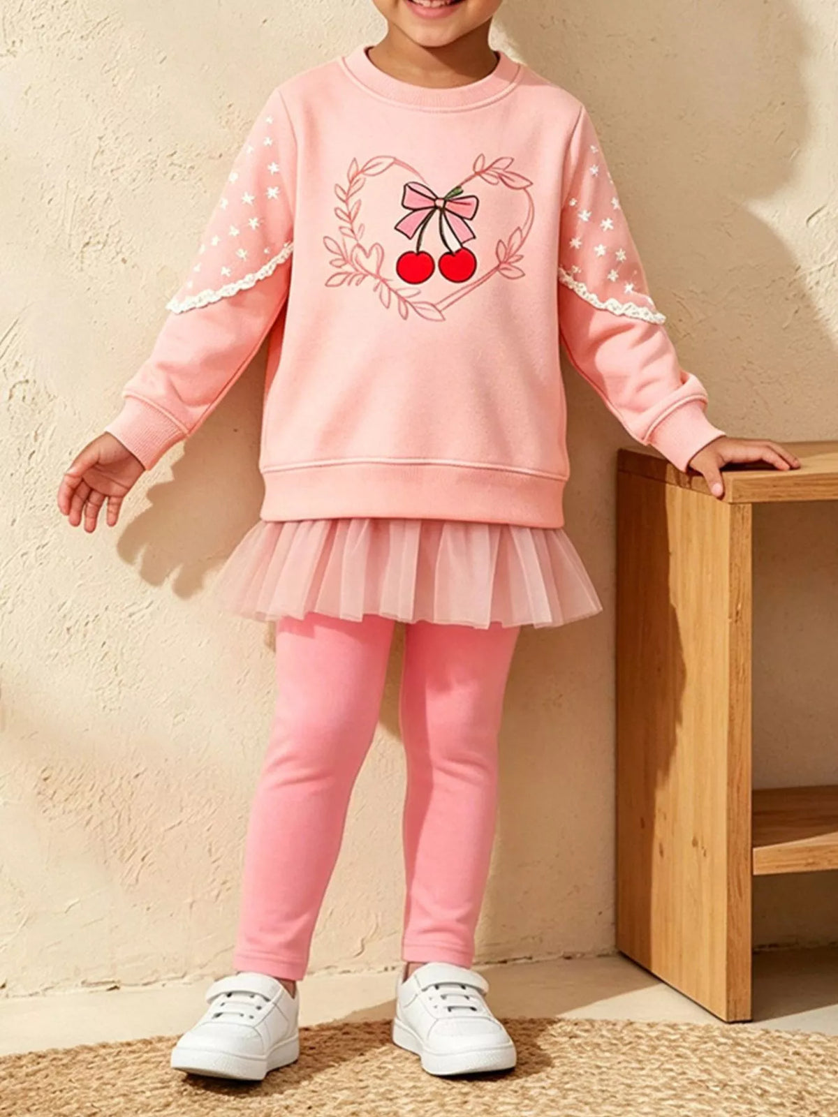 Mädchen in rosa Sweatshirt mit Kirschmotiv und Tulle-Leggings mit weißen Sternärmeln