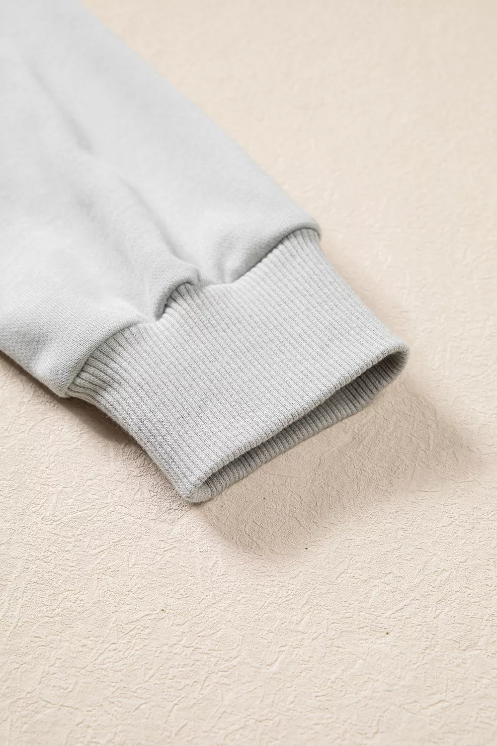 Macro shot of sleeve cuff highlighting thick, textured ribbed knit elastic band in matching light grey fabric resting on a