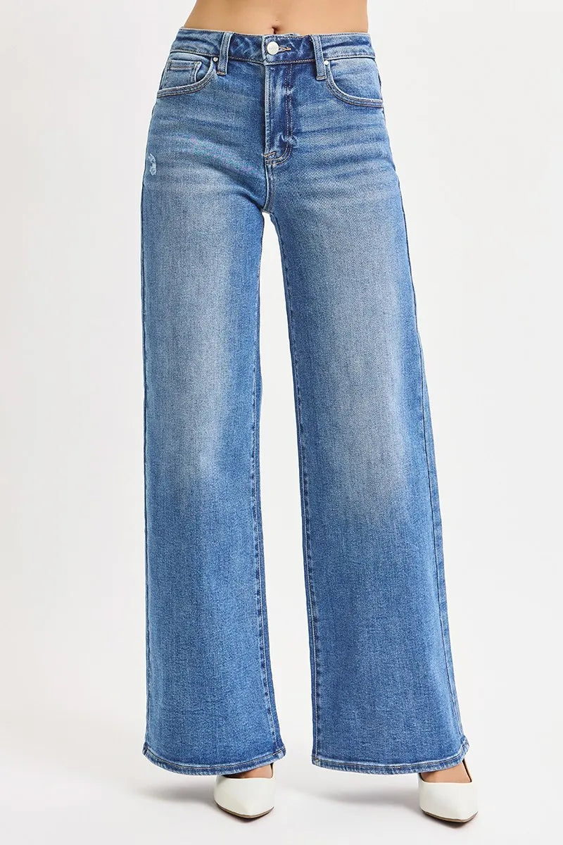 Plus-size medium wash denim showing symmetrical leg flare, belt loops, and fading hem paired with white pointed shoes