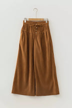 Plano frontal de pantalones de pana camel colgados, mostrando tapeta con botones y detalles de pliegues en la tela