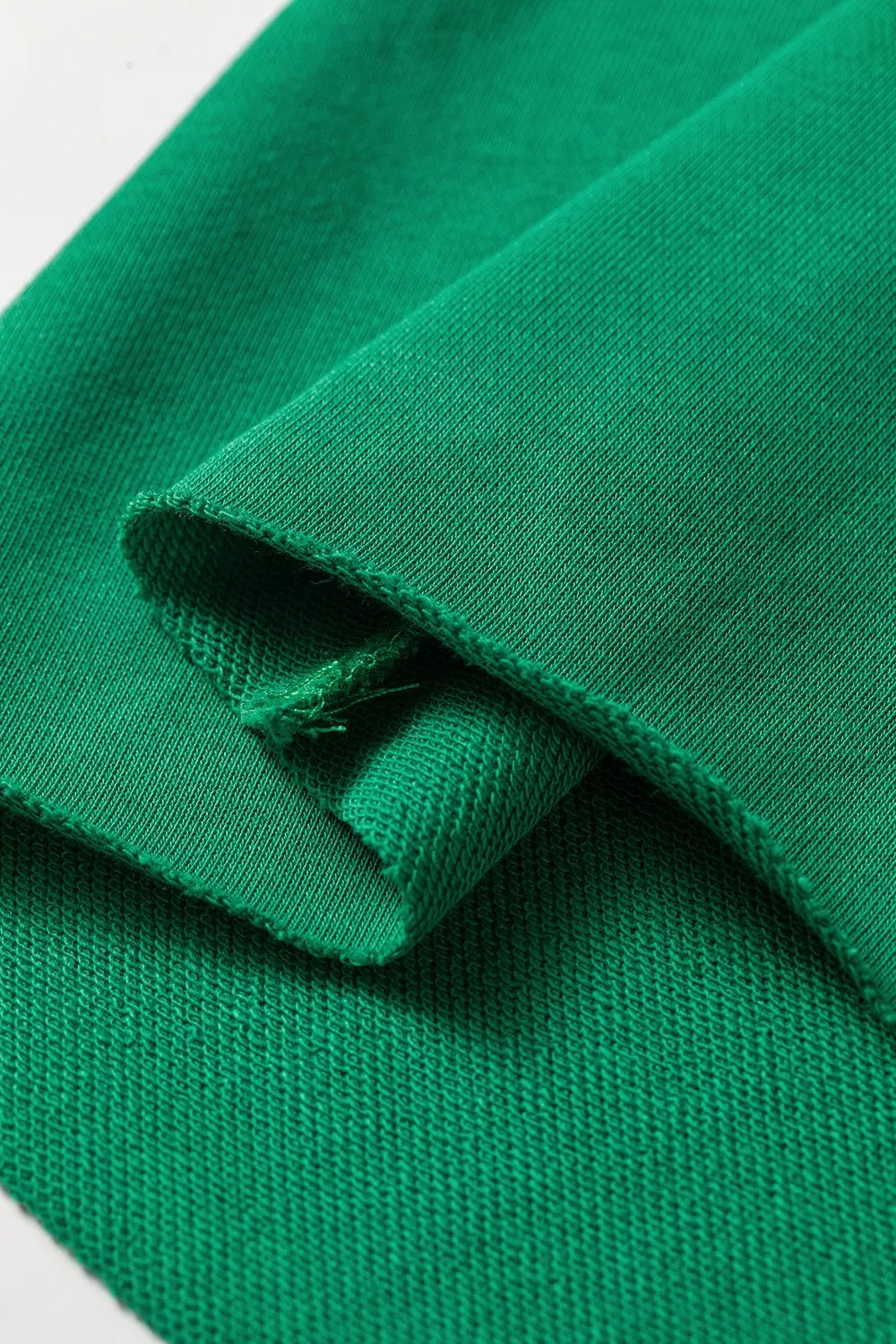 Macro extremo del borde de tela verde revelando patrón de punto bucle intrincado y estructura de tejido resistente.