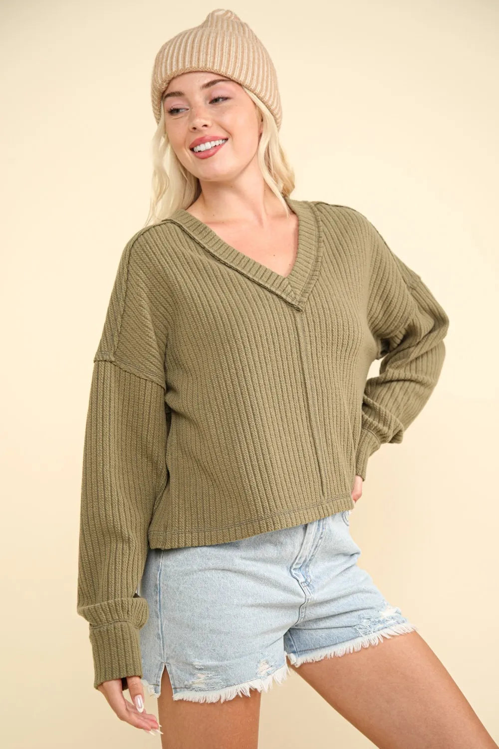 Olive green ribbed knit top with V-neck exposed seams and dropped shoulders worn by a model against a cream background