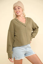 Olive green ribbed knit top with V-neck exposed seams and dropped shoulders worn by a model against a cream background