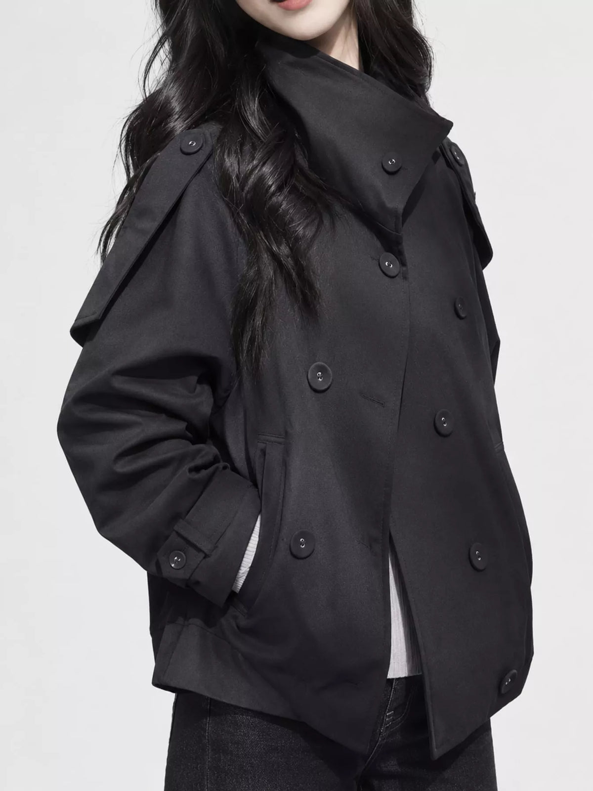 Model in schwarzem, doppeltreihigem Crop-Trench posiert mit Hand in schräger Tasche vor weißem Hintergrund