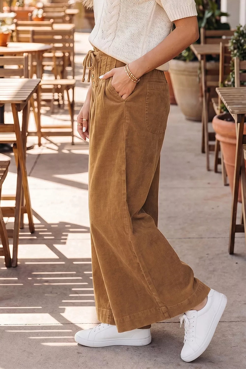 Perfil lateral de modelo caminando con pantalones de pana camel hasta el tobillo, combinados con top de punto crema