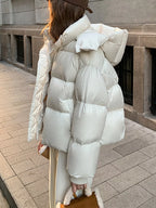 Rear view of model in cream puffer jacket emphasizing voluminous hood and horizontal quilting pattern