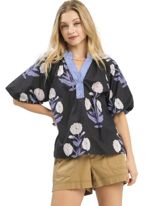 Black puff sleeve blouse with white and lavender floral print, light blue V-neck placket with striped trim, worn by model
