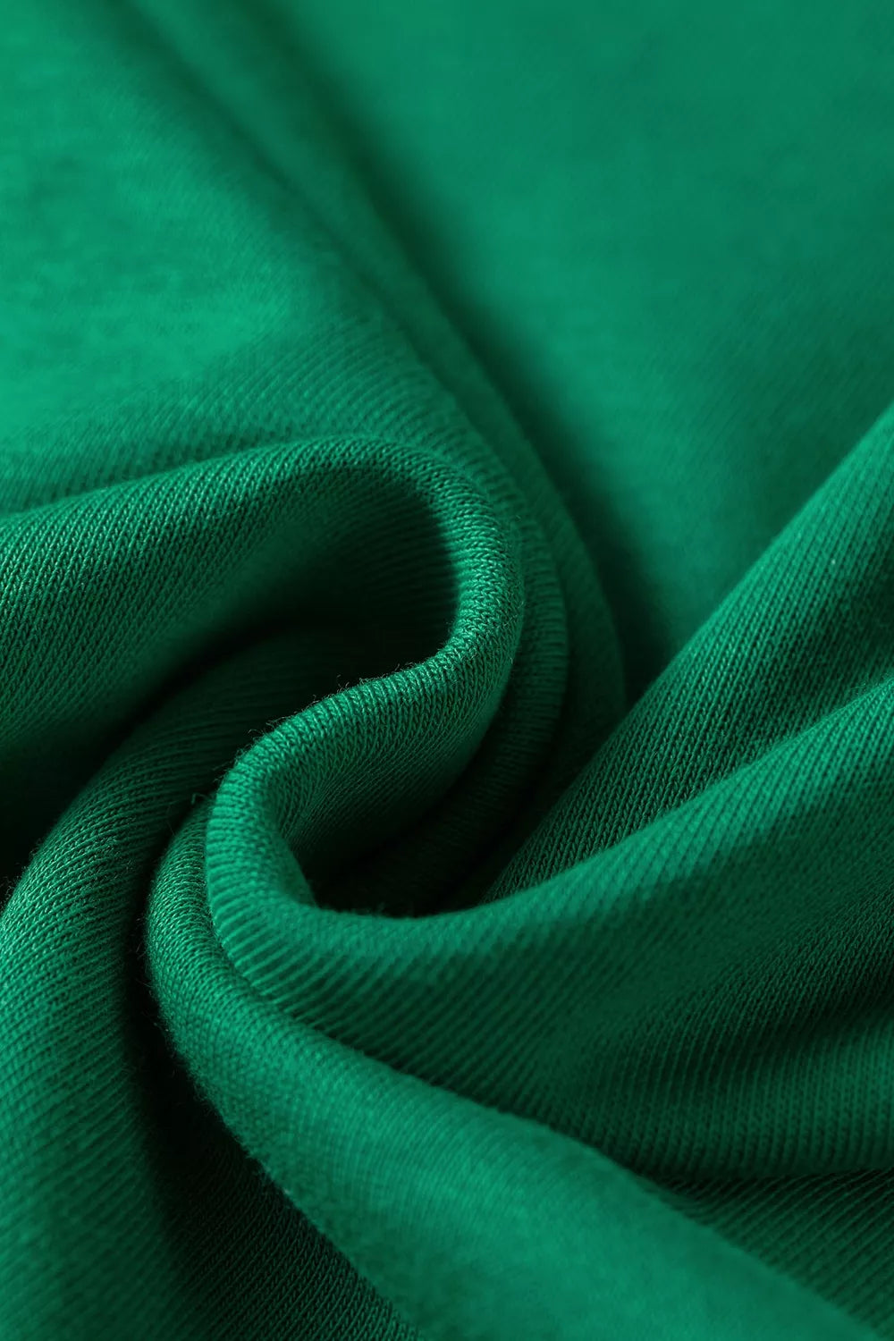 Primer plano artístico de tela verde esmeralda caída, mostrando pliegues suaves, textura de punto fina y color rico.