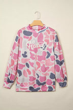 Pink grey camouflage pullover on wooden hanger showing ribbed mock neck and elastic cuffs