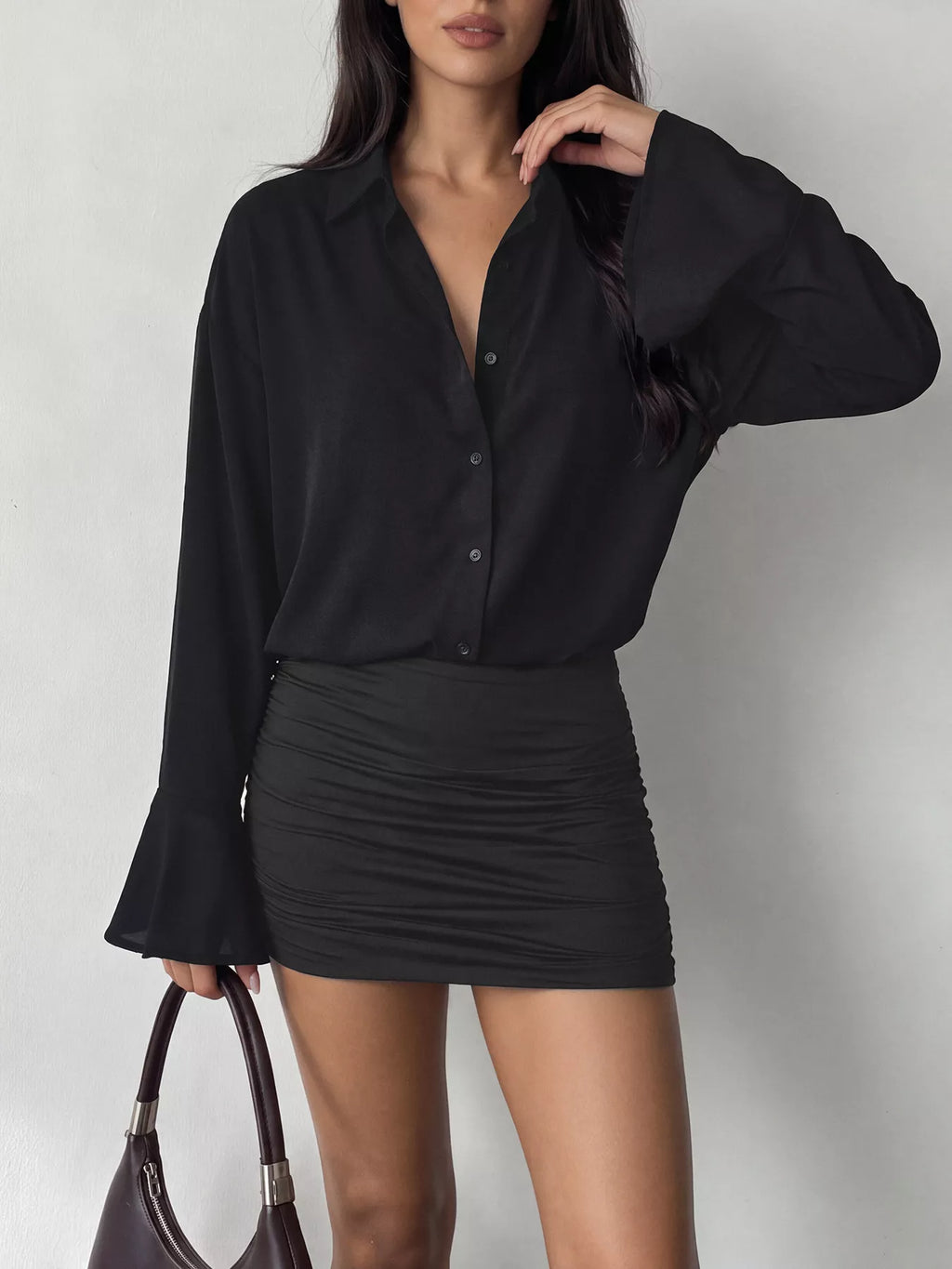 Plan moyen haut corsage robe noire : bouton devant ouvert et volants drapés près d'un sac