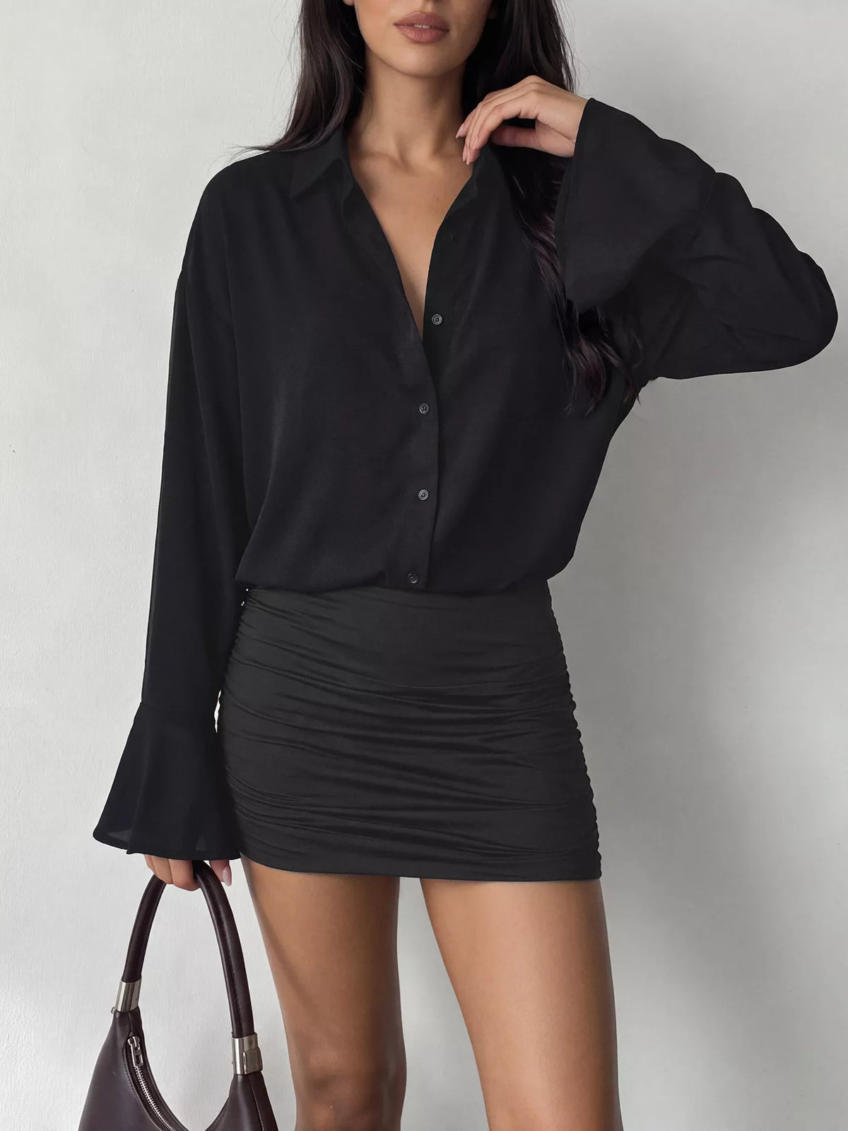 Plan moyen haut corsage robe noire : bouton devant ouvert et volants drapés près d'un sac