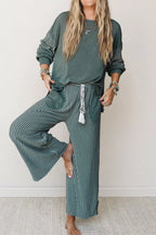 Barfüßiges Model posiert im teal gestreiften Lounge-Set, zeigt fließenden Stoff und oversized Patchwork-Top-Passform