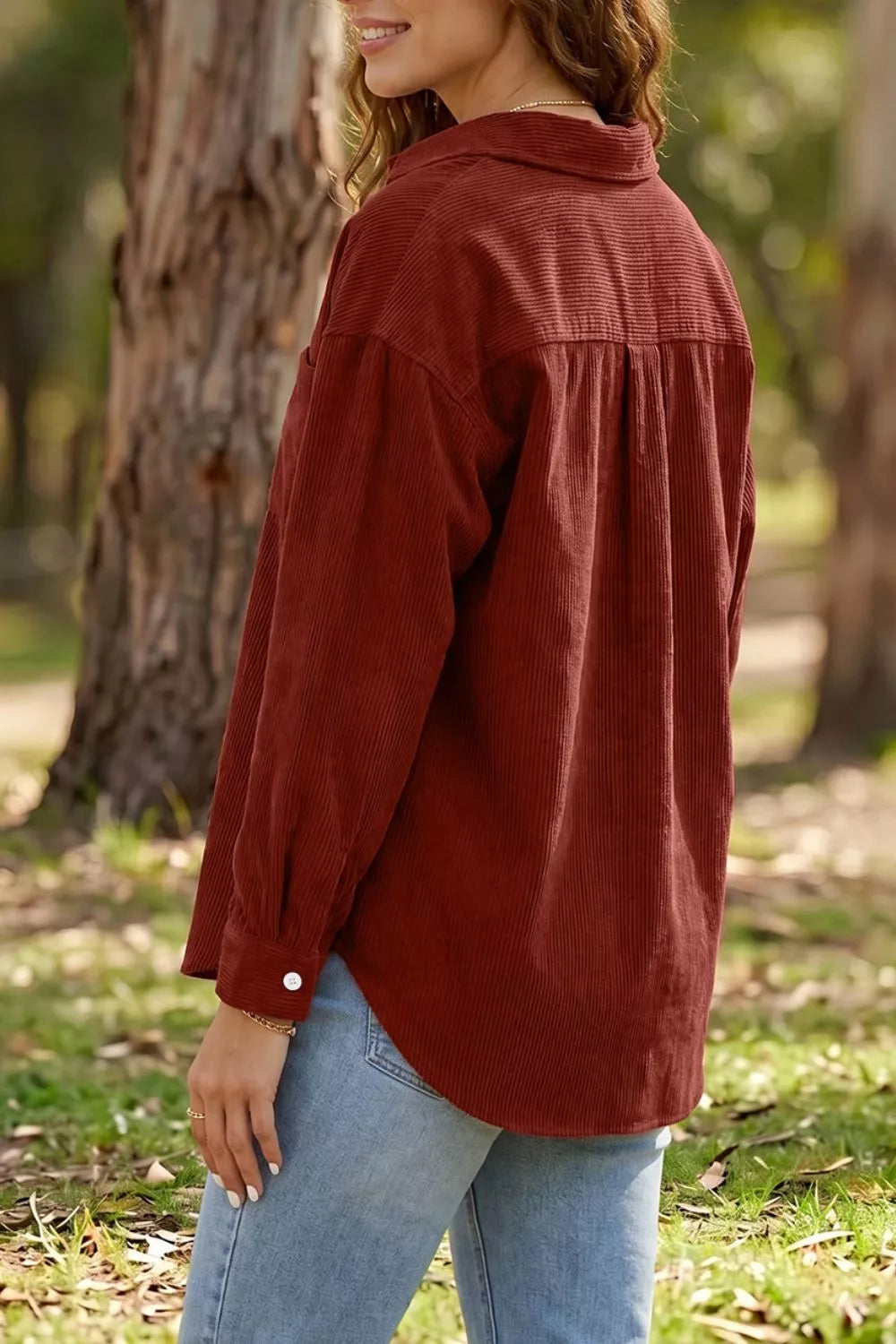 Three-quarter rear view of rust corduroy shirt draping over denim jeans in woods