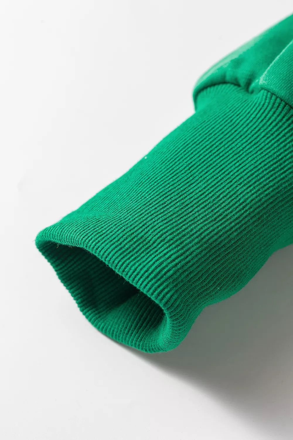 Macro del puño acanalado verde, resaltando textura de punto vertical. Diseño cómodo y estilo relajado para mujer.