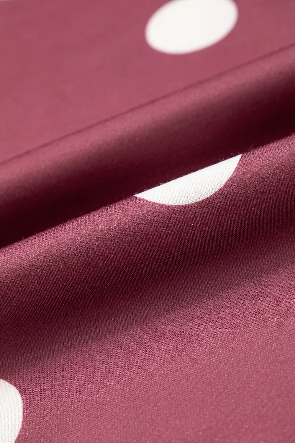 Macro view of smooth burgundy polyester knit fabric surface with large white circular dot pattern