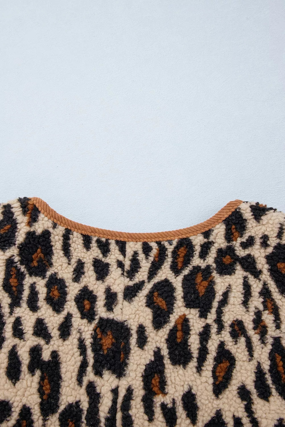 Macro close-up of cream and black leopard plush texture and precise stitching of brown corduroy trim