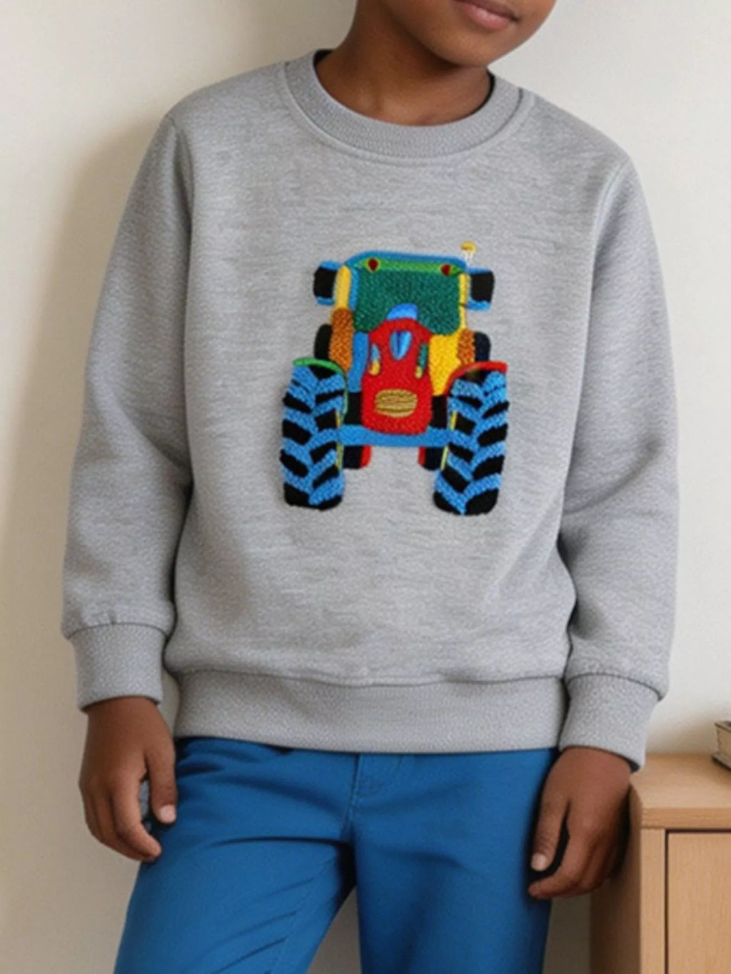 Kind in heathergrauem Baumwoll-Sweatshirt mit rotem und blauem Stickerei-Traktor-Motiv auf der Brust