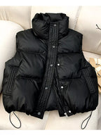 Black quilted puffer vest with snap buttons and drawstring hem on cream sofa