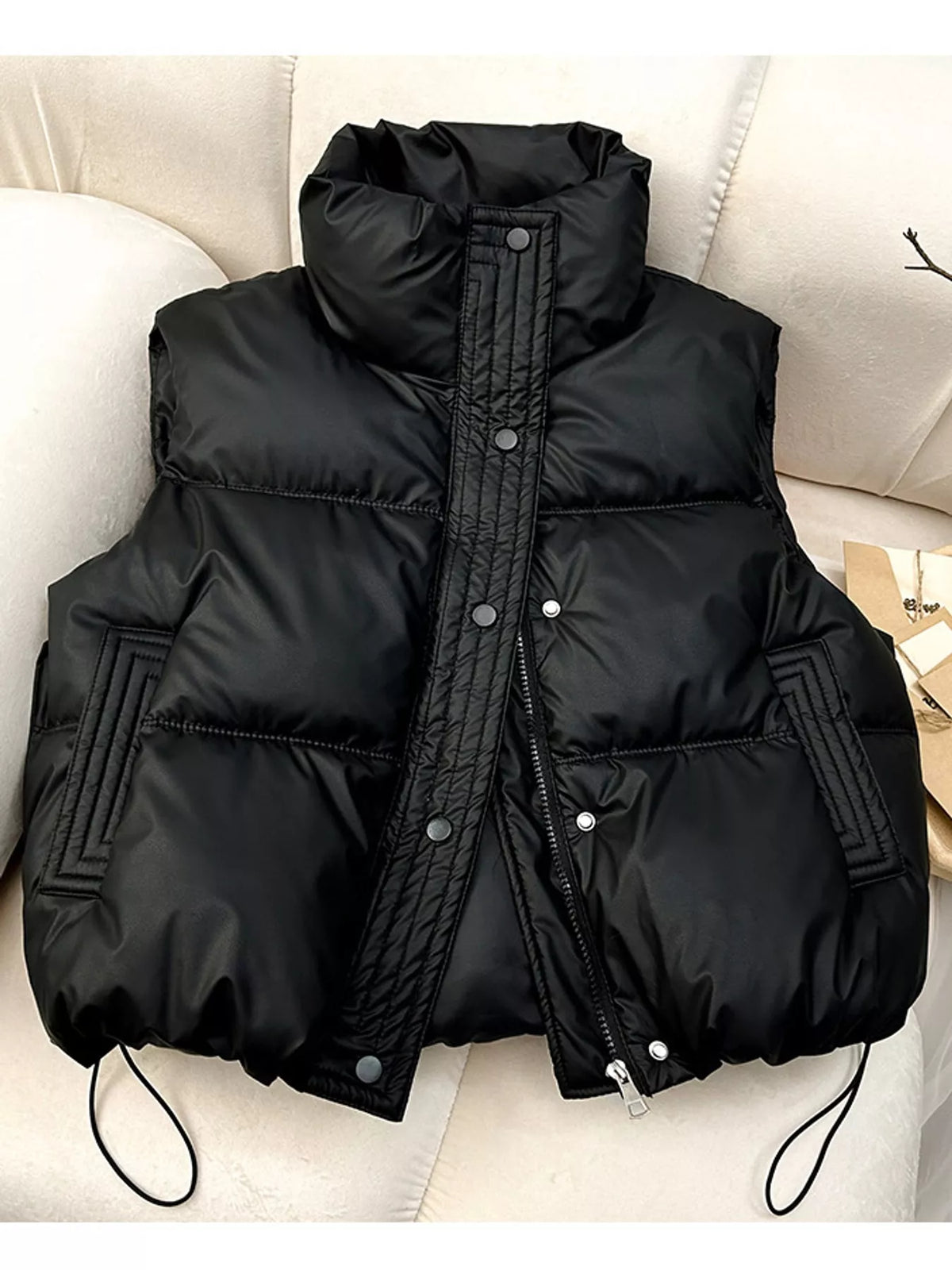 Black quilted puffer vest with snap buttons and drawstring hem on cream sofa