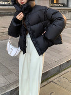 Woman wearing black quilted puffer with hood up, carrying white crescent bag for street style look