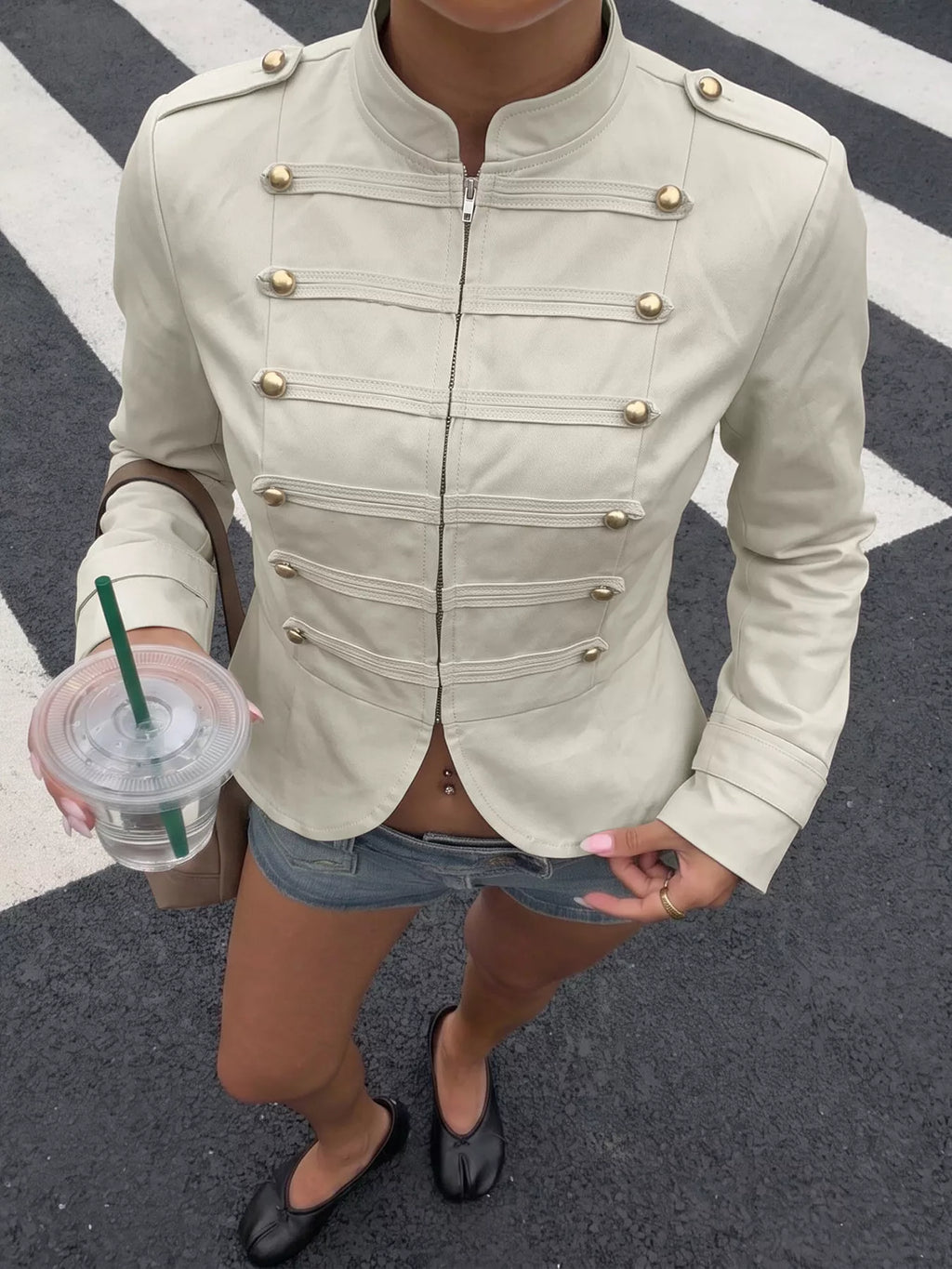 Veste cropped beige clair à col mandarin et fermetures pression dorées portée par un modèle en extérieur