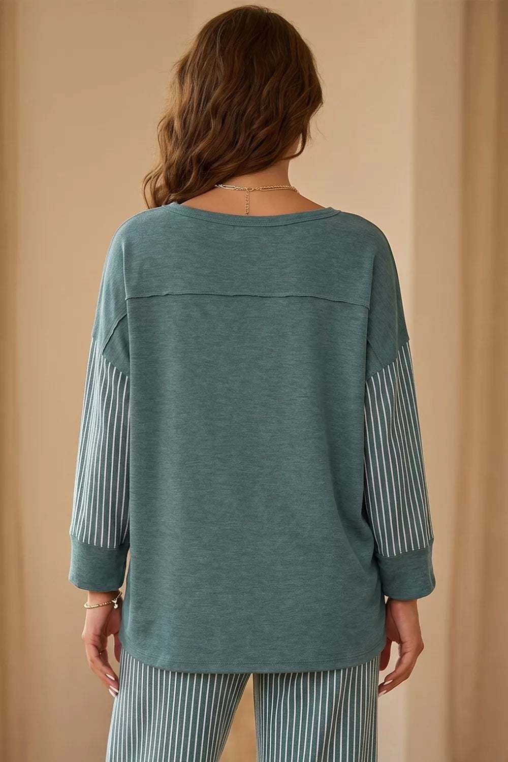 Rückansicht des teal Langarmtops mit horizontaler Naht und weißen Streifenärmeln vor beige Hintergrund