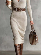 Modèle portant une robe tricotée côtelée beige à col V, manches longues, ceinture boucle argentée, bottes western et sac main sur fond gris