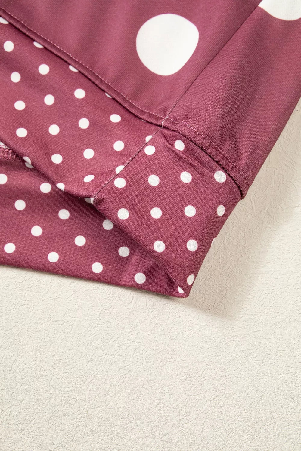 Hem band detail where large polka dot print meets dense smaller white dots on maroon polyester fabric